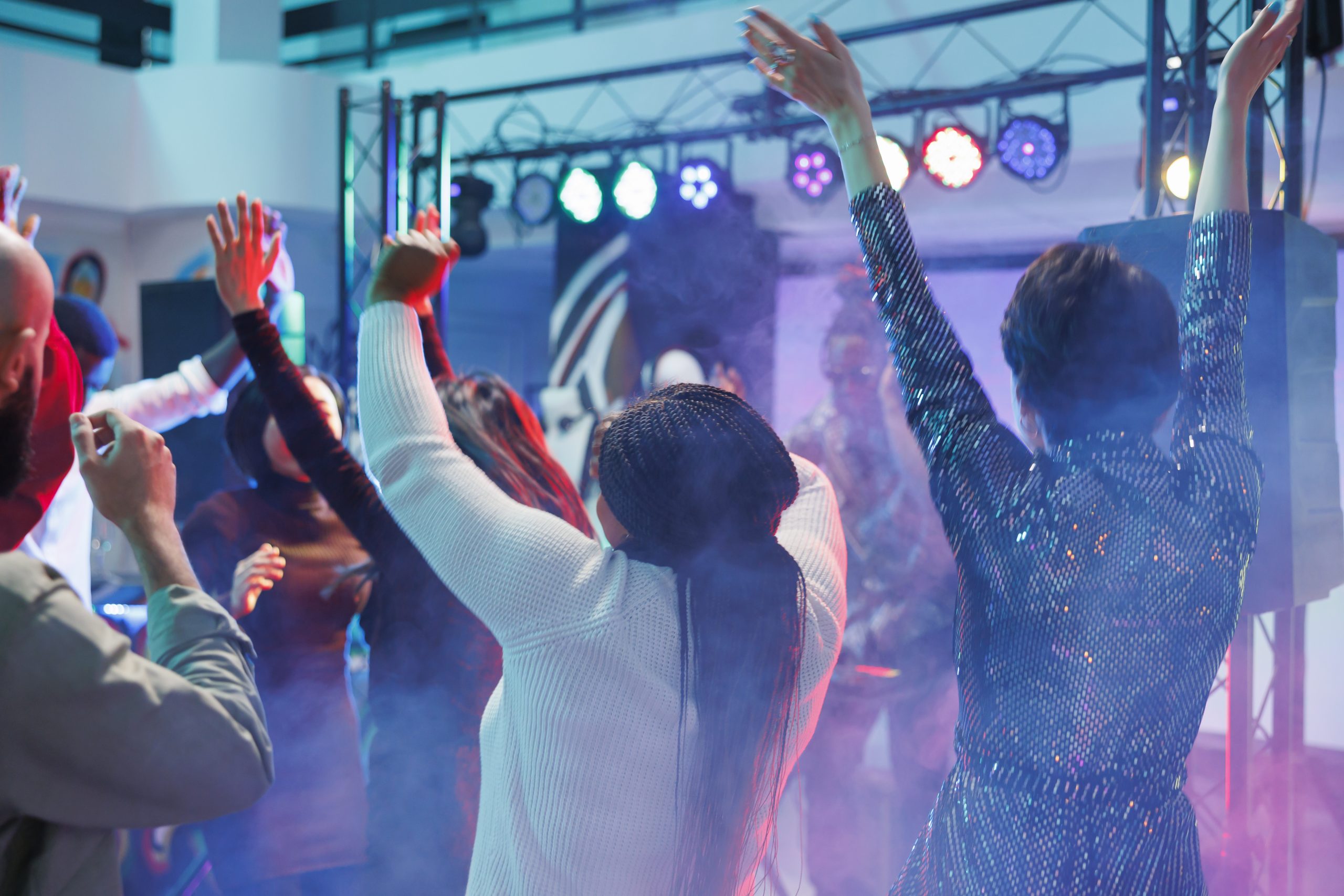 People partying and raising hands while moving to electronic music rhythm on dancefloor. Diverse friends dancing and enjoying nightlife activity while attending dj performance in nightclub